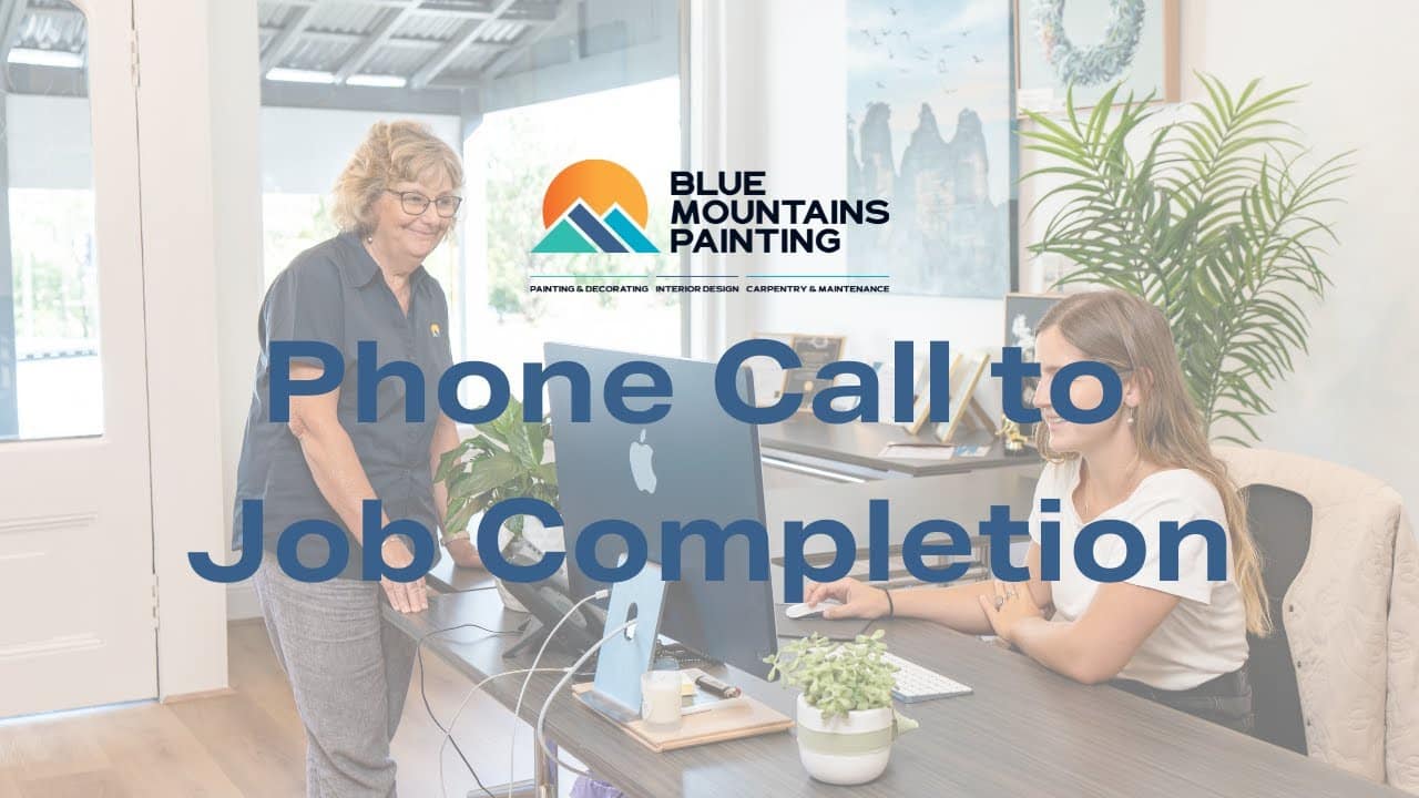 Two women work at desks in a modern office with Blue Mountains Painting branding, highlighting their expertise from "Phone Call to Job Completion," including restoration and heritage painting services.