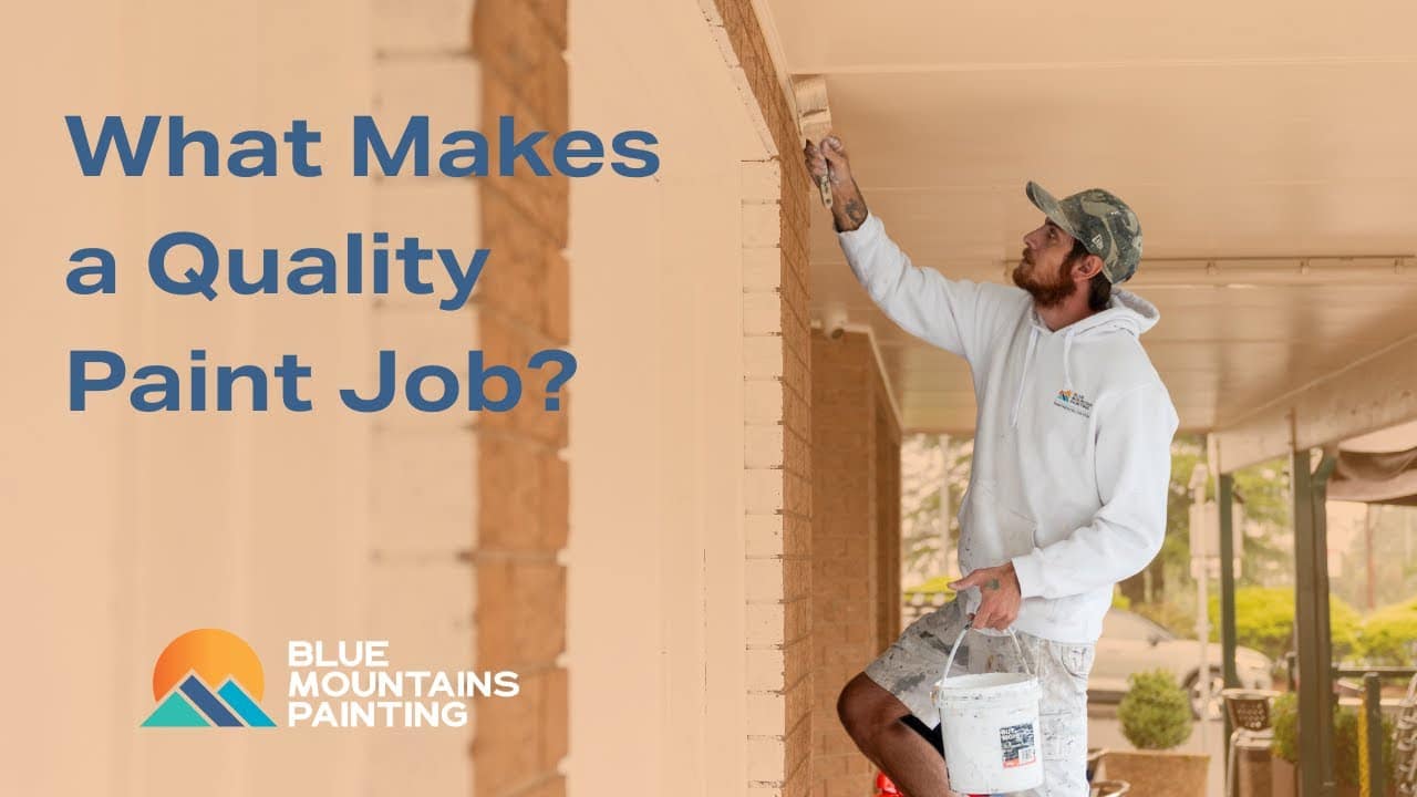 A man in a white hoodie paints the exterior of a house; text reads "What Makes a Quality Paint Job?" with the Blue Mountains Painting logo, highlighting expert painting services.