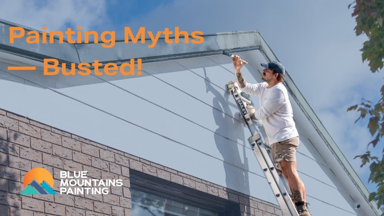A man stands on a ladder painting the trim of a house; text reads "Painting Myths — Busted!" and "Blue Mountains Painting" with a mountain logo, sharing helpful Painting Tips for your next project.