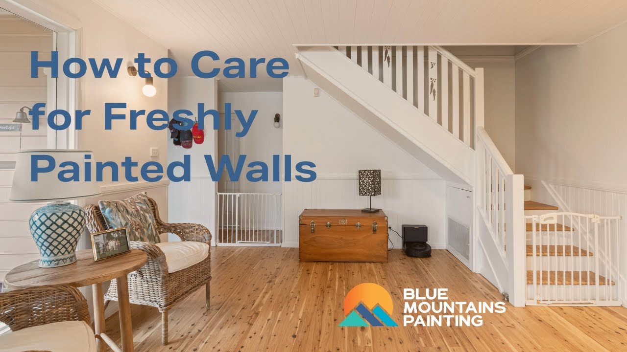 A clean, modern living room with freshly painted walls, wooden floor, and staircase. Text reads "How to Care for Freshly Painted Walls" and "Blue Mountains Painting" with logo—perfect tips for wall care and paint maintenance.